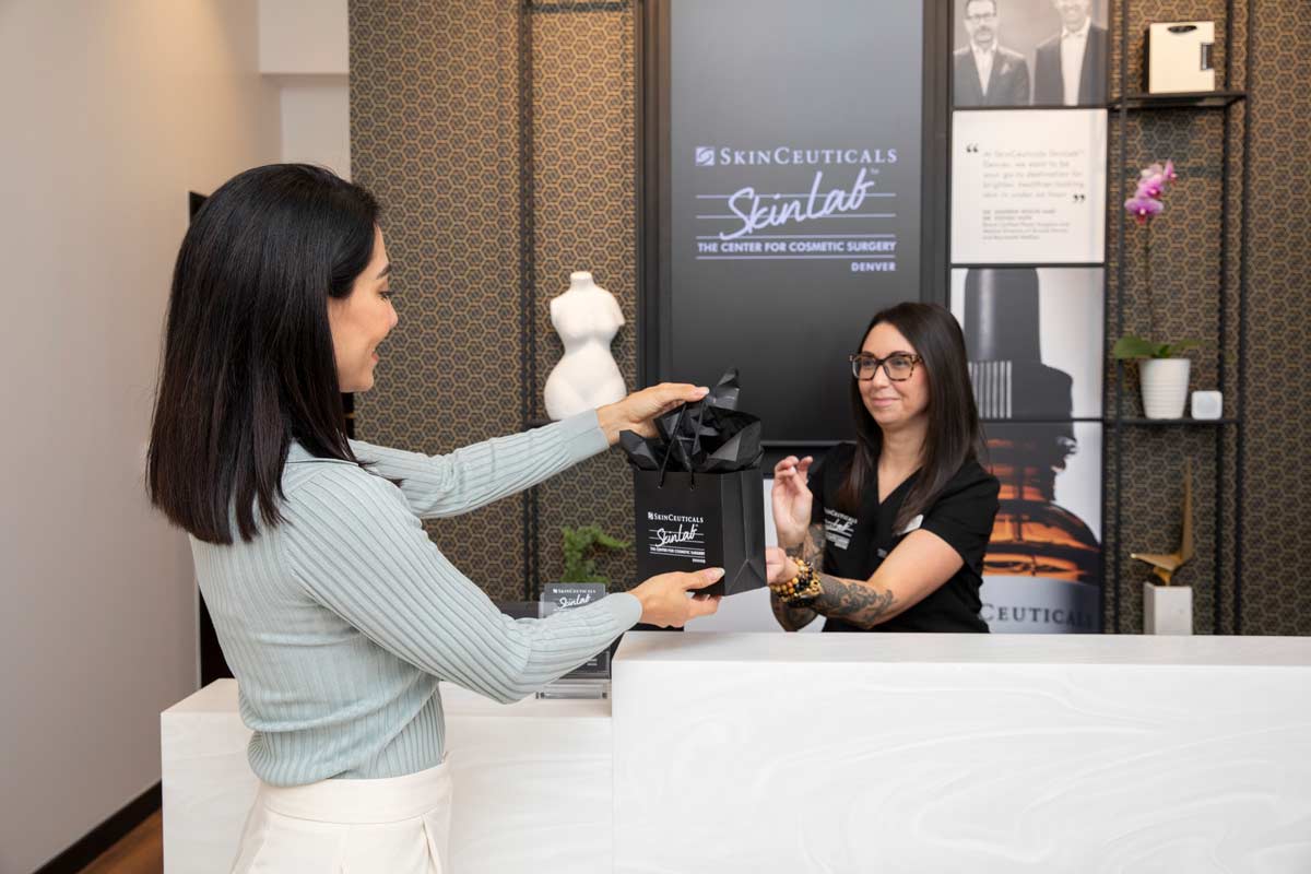 Front desk staff presenting a SkinCeuticals skincare gift bag to a patient.
